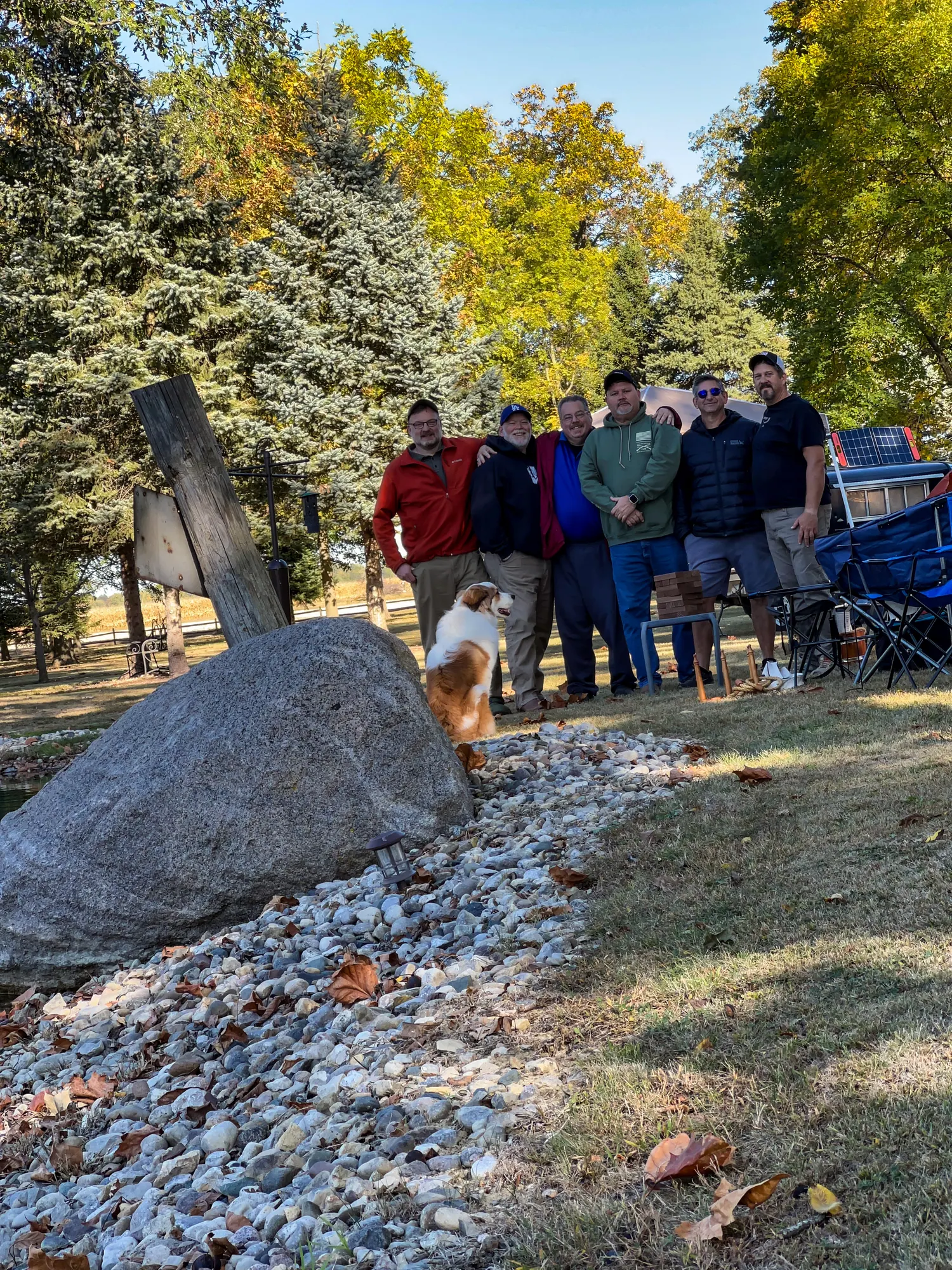 The group gathered together with a dog by the big boulder at the pond's edge on a sunny fall afternoon.