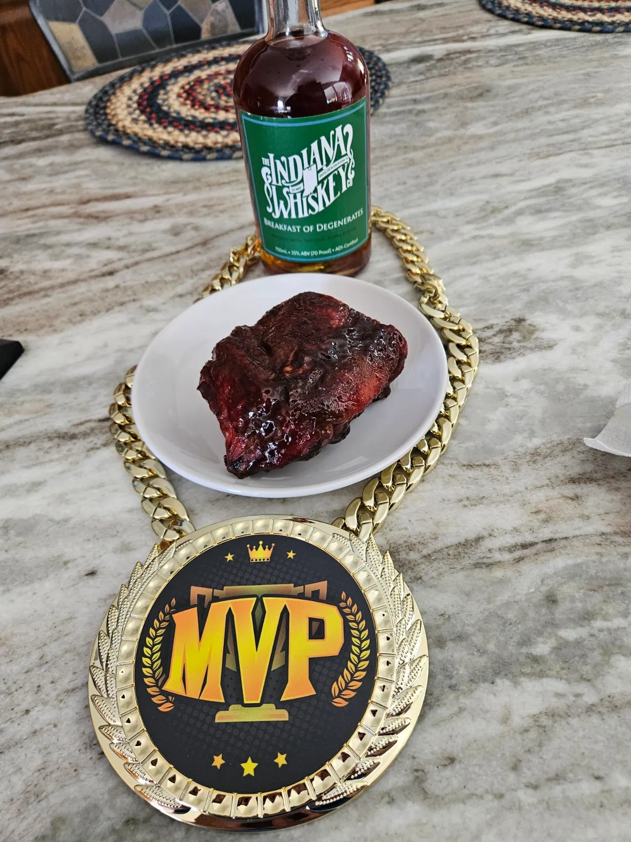 A bottle of Indiana Whiskey, a plate of glazed smoked pork, and a gold MVP champion medal on the table.