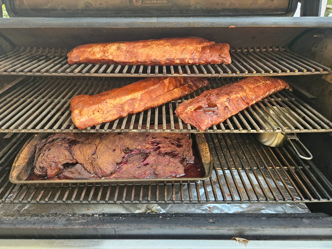 Three racks of ribs and a brisket cooking on the racks of a pellet smoker.